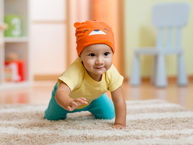Little kid with a cute orange beanie crawling on carpet